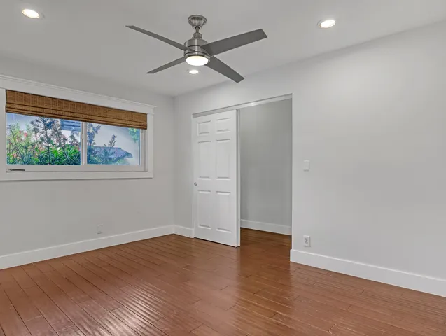 an empty room with wooden floor chandelier fan and windows