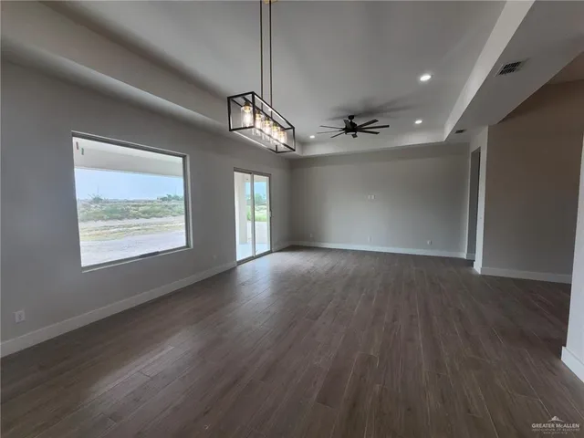 an empty room with wooden floor chandelier and windows