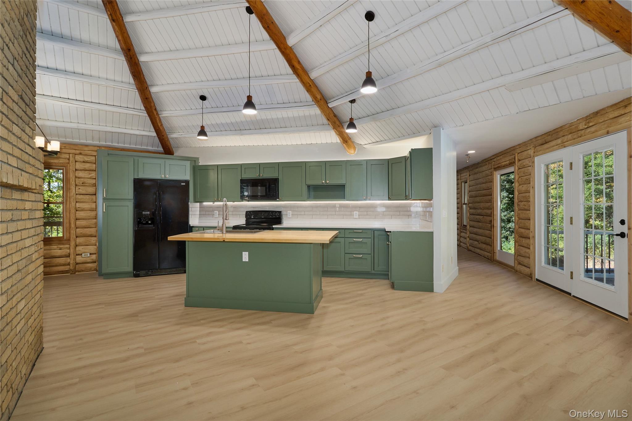 568 Oak Summit Road Millbrook, NY 12545 - Photo 19 of 50 Kitchen with green cabinetry, rustic walls, light wood finished floors, black appliances, and a center island with sink