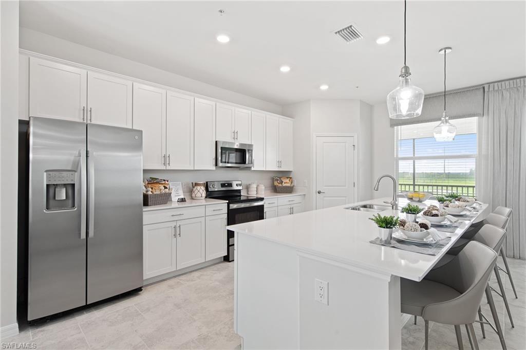 6008 Ellerston Way Avenue, Unit 1021 Immokalee, FL 34142 - Photo 14 of 50 Kitchen featuring appliances with stainless steel finishes, white cabinetry, a center island with sink, a kitchen breakfast bar, and pendant lighting