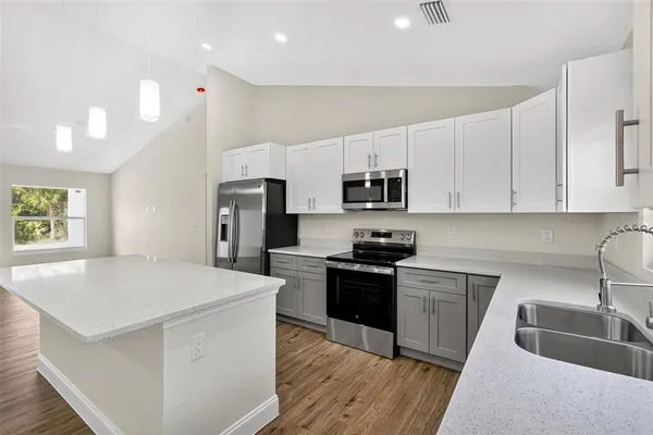 a large kitchen with stainless steel appliances granite countertop a stove top oven a sink dishwasher and white cabinets with wooden floor