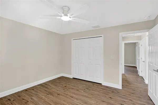 an empty room with wooden floor chandelier fan and windows