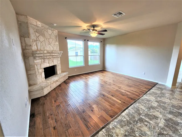 a view of an empty room with wooden floor fireplace and a window