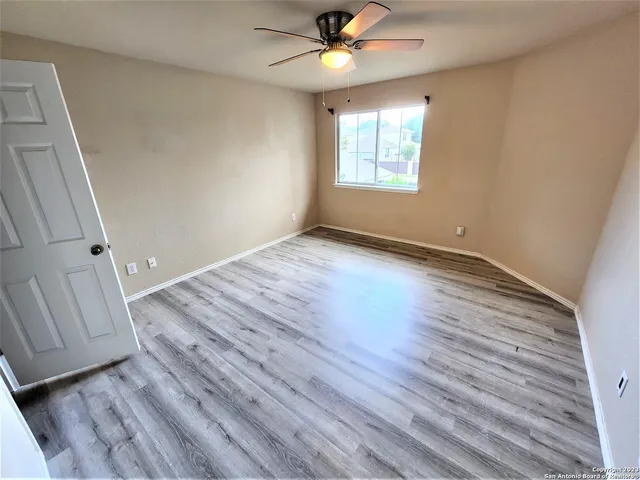 an empty room with wooden floor fan and windows