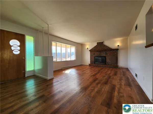 an empty room with wooden floor fireplace and windows