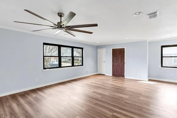 an empty room with wooden floor fan and windows