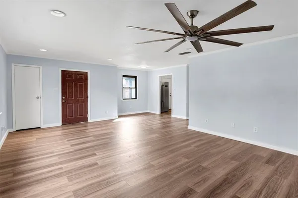 a view of an empty room with wooden floor and a ceiling fan