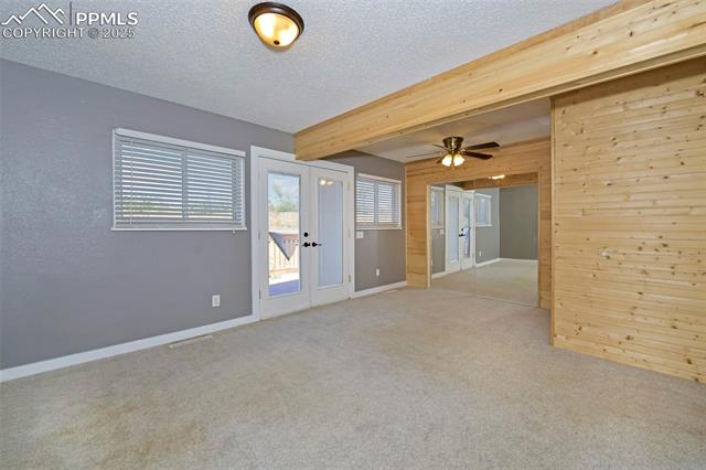 1914 Wooten Road Colorado Springs, CO 80915 - Photo 16 of 39 Carpeted spare room with french doors, wooden walls, a textured ceiling, beamed ceiling, and ceiling fan