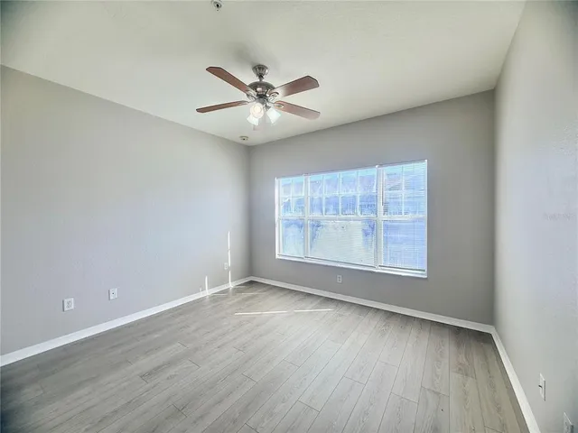 an empty room with wooden floor fan and windows