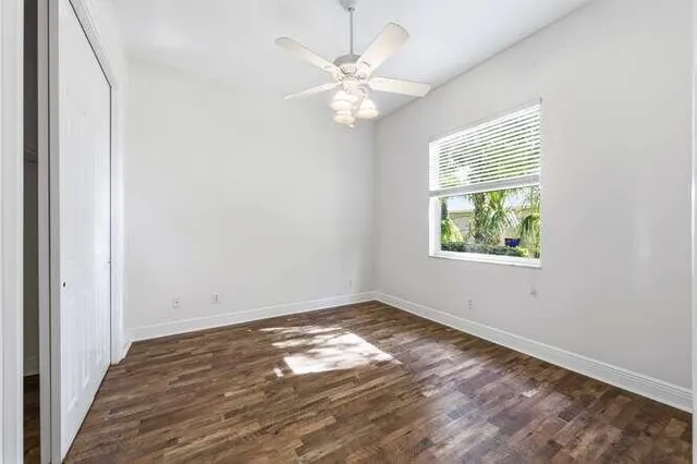 an empty room with wooden floor chandelier fan and windows