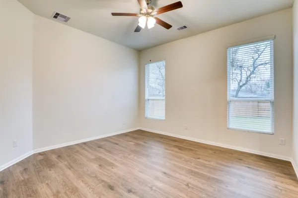 an empty room with wooden floor fan and windows