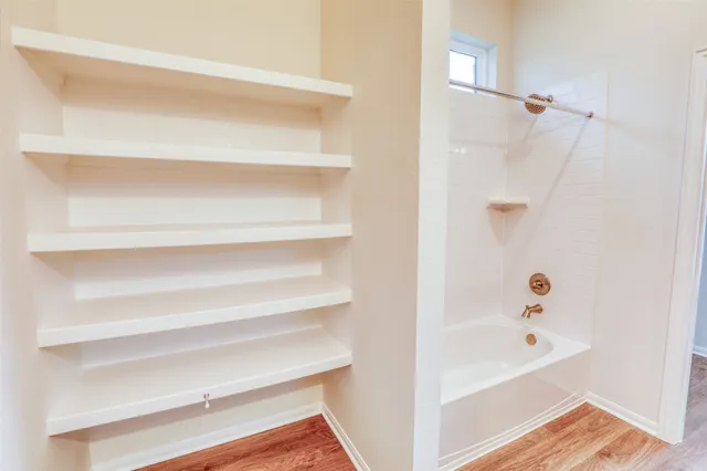 a view of a hallway with wooden floor and a bathroom