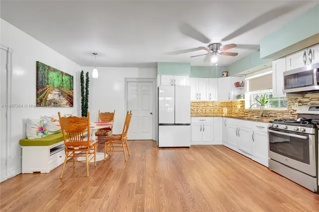 a open kitchen with stainless steel appliances granite countertop a stove top oven a refrigerator a dining table and chairs with wooden floor