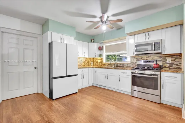 a kitchen with granite countertop a refrigerator oven a sink dishwasher and white cabinets with wooden floor