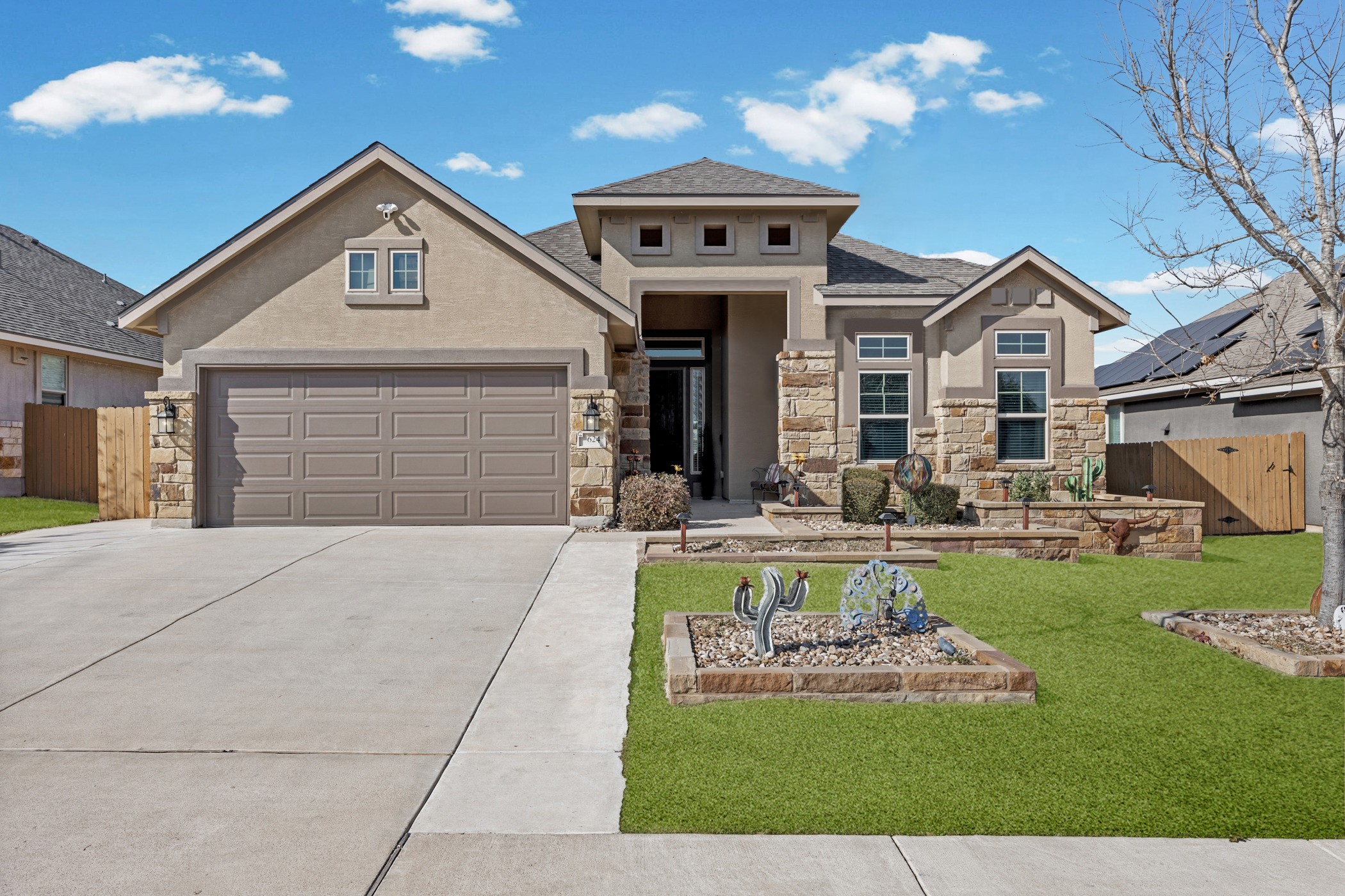 View of front of house featuring stone siding, driveway, a gate, stucco siding, and a garage