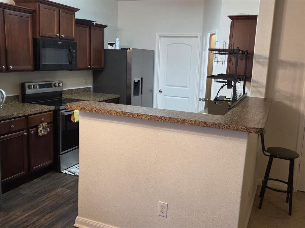 14249 Bridgeview Lane Dallas, TX 75253 - Photo 5 of 9 Kitchen featuring dark brown cabinetry, stainless steel appliances, a peninsula, a breakfast bar, and dark wood-type flooring