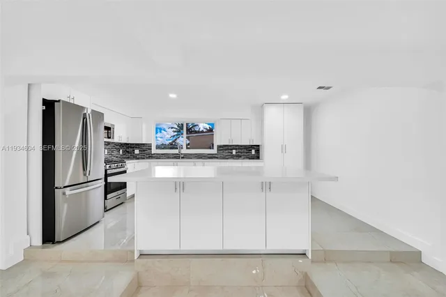 a large white kitchen with kitchen island a sink stainless steel appliances and cabinets