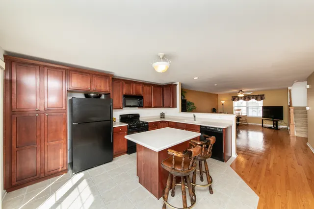 a kitchen with stainless steel appliances kitchen island granite countertop a refrigerator a stove a sink a dining table and chairs with wooden floor