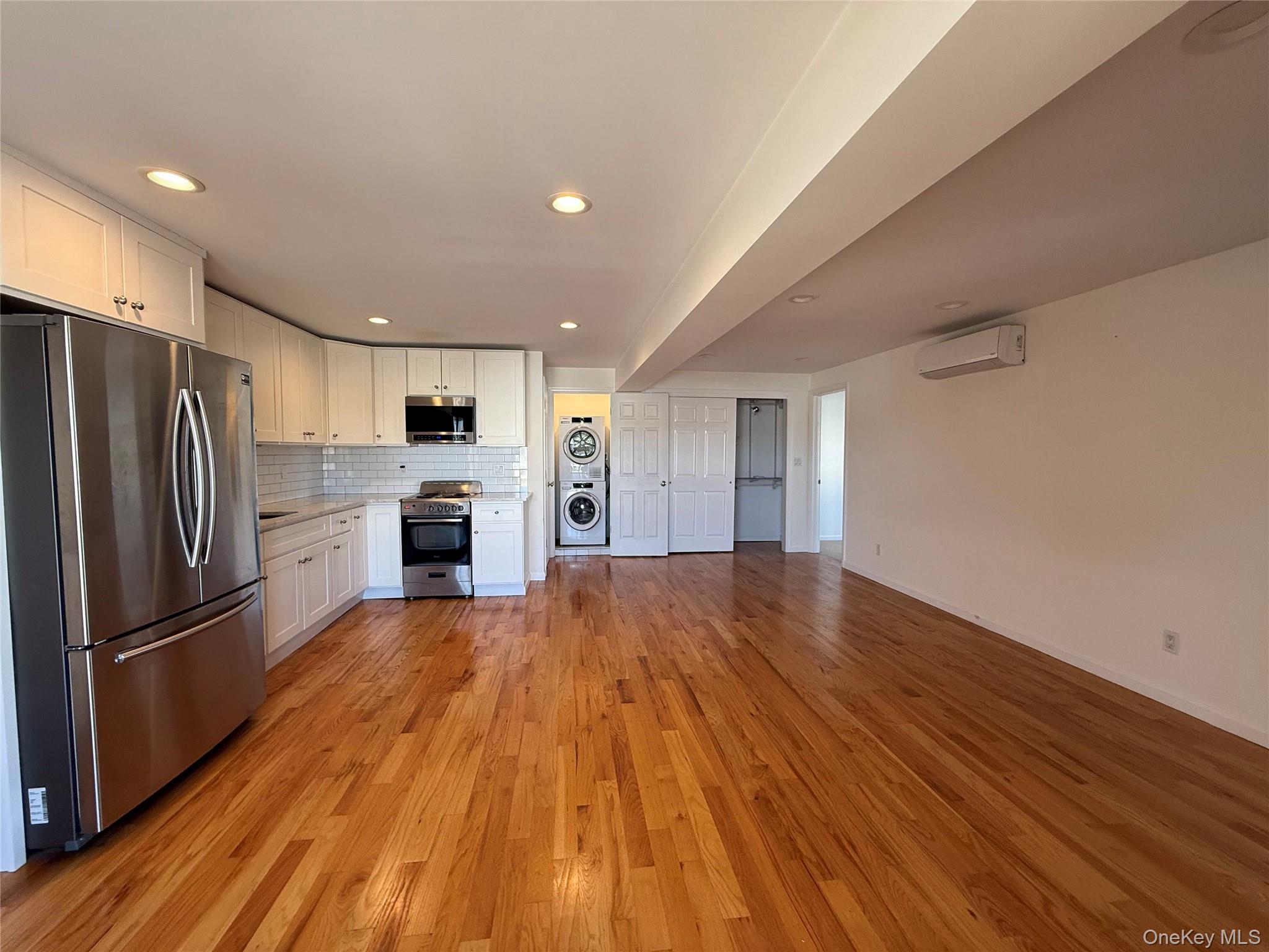 505 South Main Street Freeport, NY 11520 - Photo 9 of 10 Kitchen featuring appliances with stainless steel finishes, white cabinets, backsplash, light wood finished floors, and stacked washing machine and dryer