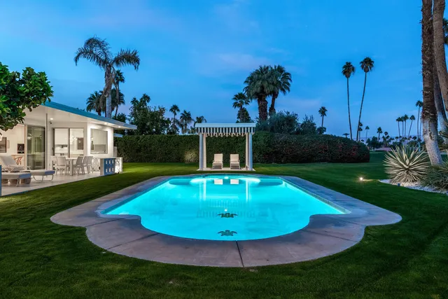 a view of a swimming pool with a yard and palm trees