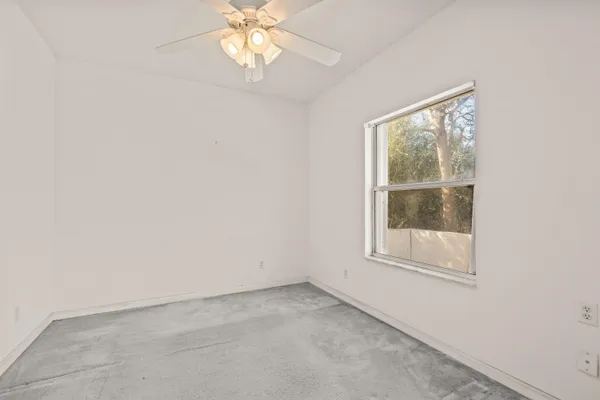 an empty room with chandelier fan and windows