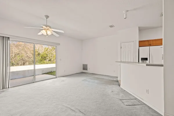 an empty room with a ceiling fan and kitchen view