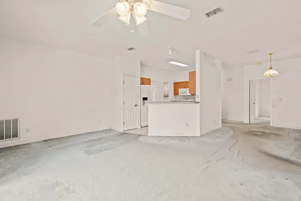 an empty room with chandelier fan and kitchen view
