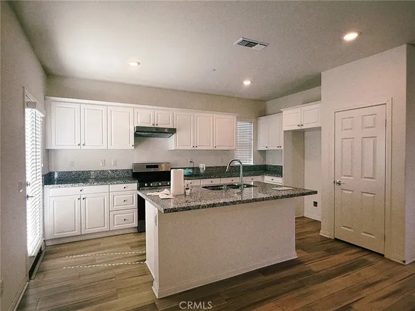 a kitchen with stainless steel appliances granite countertop a stove a sink dishwasher a refrigerator and white cabinets with wooden floor