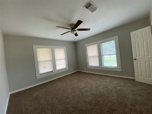 an empty room with chandelier fan and windows