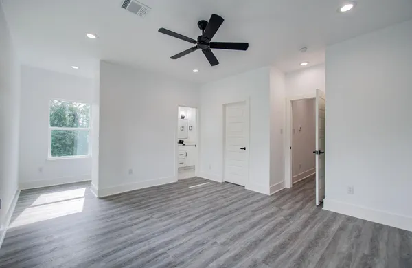 an empty room to hallway with wooden floor a ceiling fan and windows