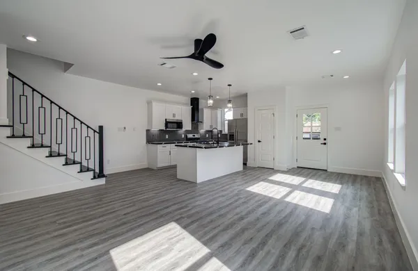 a view of an empty room and kitchen with wooden floor