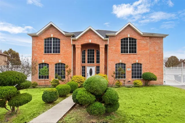 a view of a yard in front of a brick house with plants and a large tree