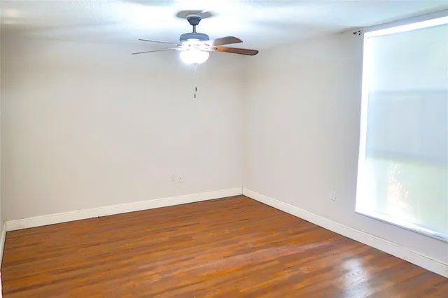 an empty room with wooden floor fan and window