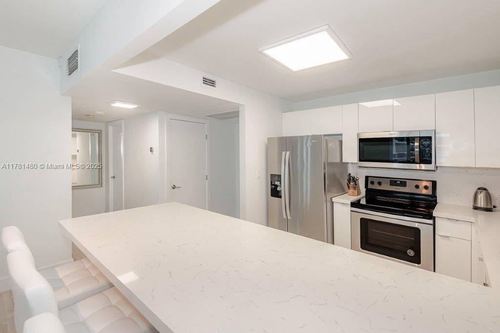 2301 Collins Avenue, Unit 401 Miami Beach, FL 33139 - Photo 21 of 38 a large white kitchen with stainless steel appliances granite countertop a stove a sink and a microwave