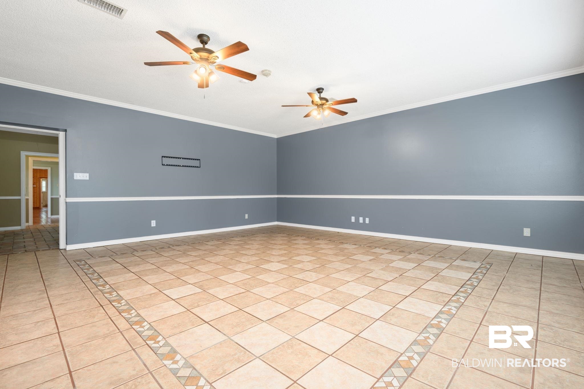 7540 2 Mile Road Irvington, AL 36544 - Photo 30 of 82 Spacious room featuring neutral tone tile flooring with decorative inlay, two ceiling fans with integrated lighting, and walls with a two-tone paint scheme and chair rail molding