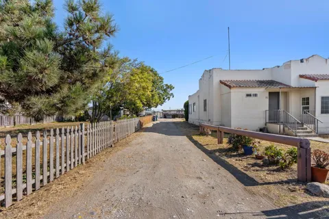 a view of a white house with a small yard and wooden fence
