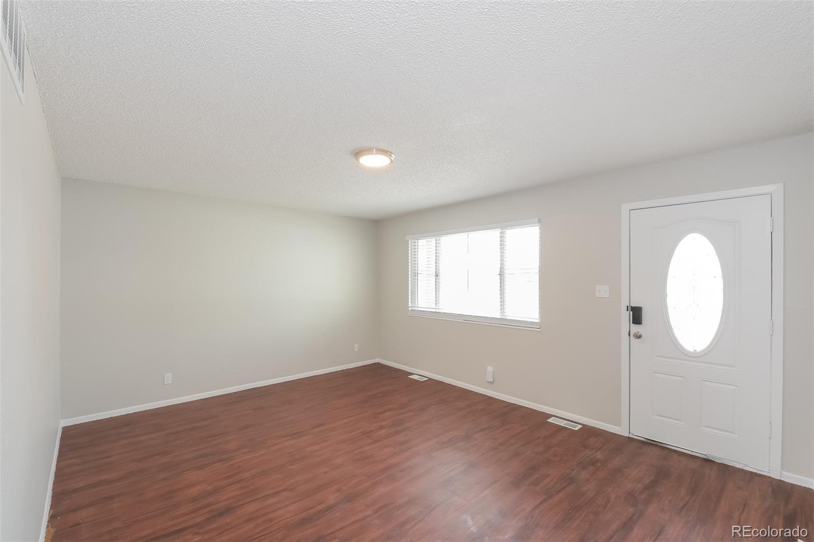 5522 Carson Street Denver, CO 80239 - Photo 4 of 17 an empty room with wooden floor and mirror