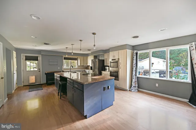 a kitchen with stainless steel appliances granite countertop a refrigerator a sink dishwasher a stove and a dining table with wooden floor