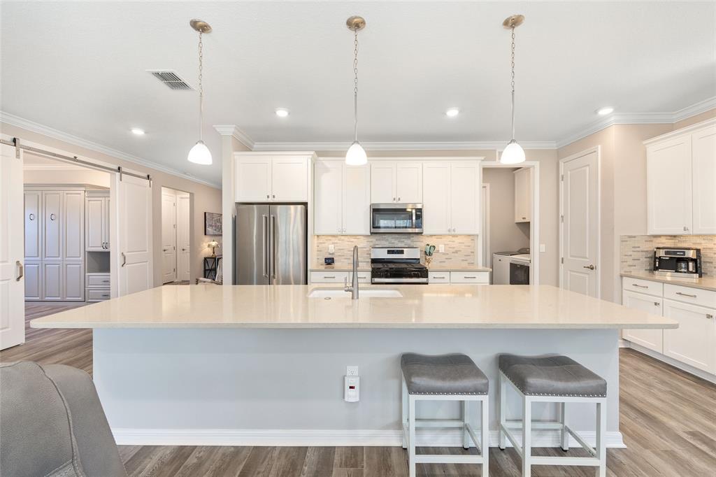 10390 Southwest 99th Street Ocala, FL 34481 - Photo 22 of 48 a large kitchen with kitchen island granite countertop a stove a sink a refrigerator and white cabinets with wooden floor