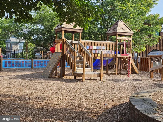 a view of a brick house in front of a yard with plants and large trees