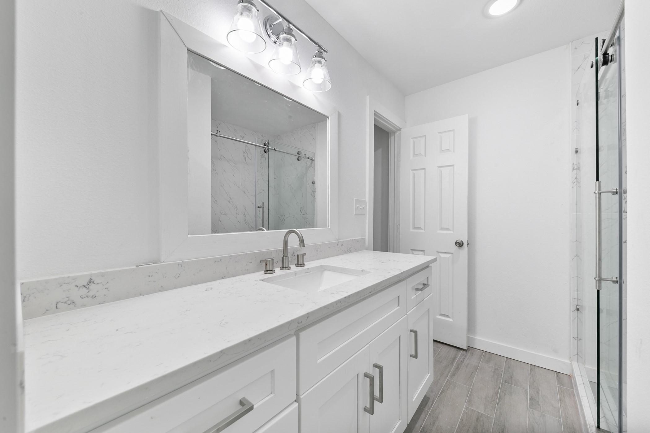 6811 McCullum Road Houston, TX 77489 - Photo 15 of 22 This bathroom features a sleek, modern design with a long white vanity, marble countertop, and integrated sink. It has a large mirror with stylish lighting and a glass-enclosed shower with marble wall accents, offering a clean and contemporary feel.