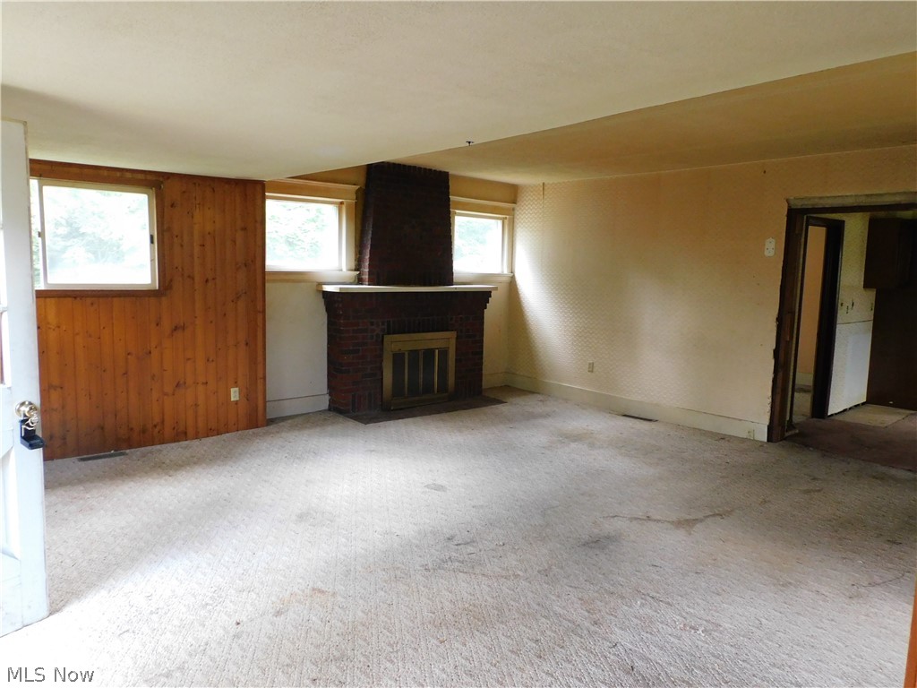 4031 South Ridge Road East Ashtabula, OH 44004 - Photo 6 of 25 Unfurnished living room featuring wood walls, light carpet, a fireplace, and brick wall