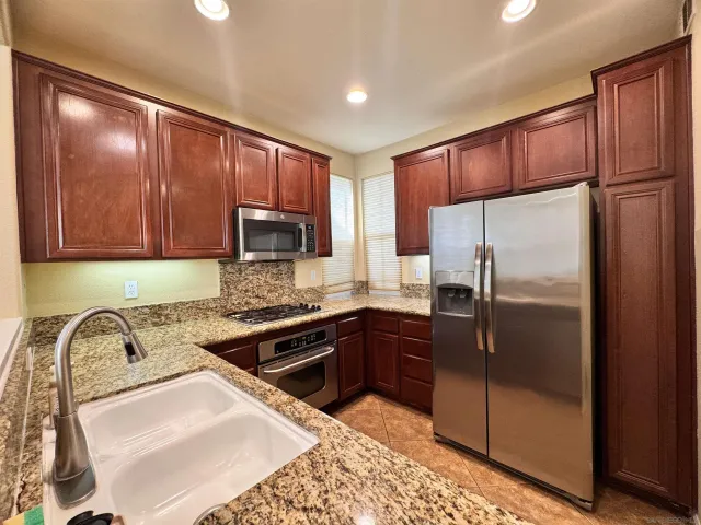 a kitchen with granite countertop stainless steel appliances a refrigerator and cabinets