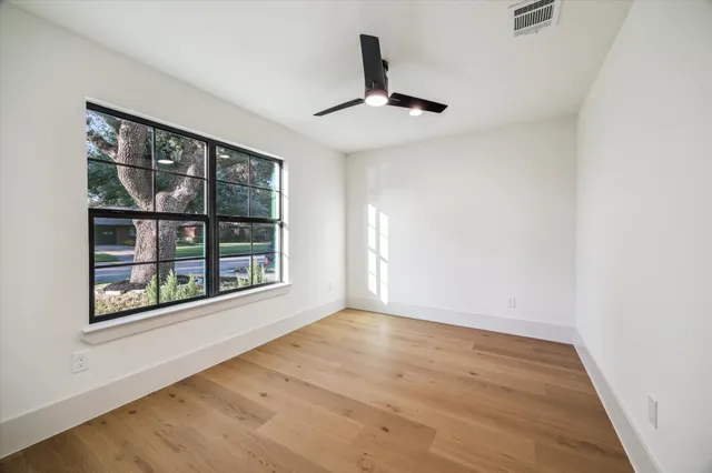 an empty room with wooden floor chandelier and windows