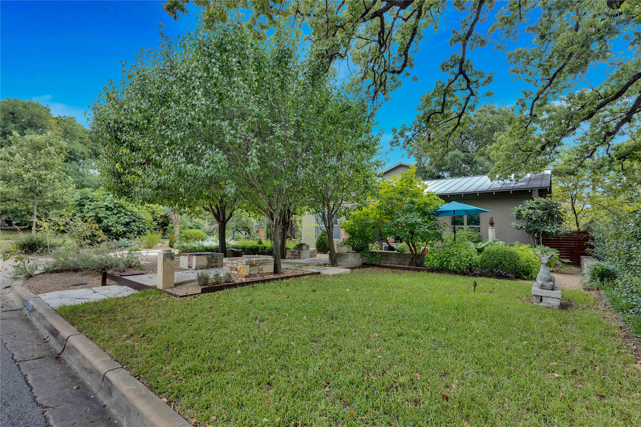 1306 Norwood Road, Unit A Austin, TX 78722 - Photo 2 of 21 Lush landscaping and mature trees enhance the inviting curb appeal of this property. The custom quality of the design makes this property truly one of a kind. This is the yard space for the house. The lawn is maintained regularly and on an irrigation system, but it is not fenced.