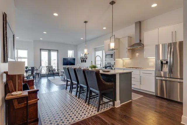 a kitchen with stainless steel appliances granite countertop a refrigerator a stove a sink a dining table and chairs with wooden floor