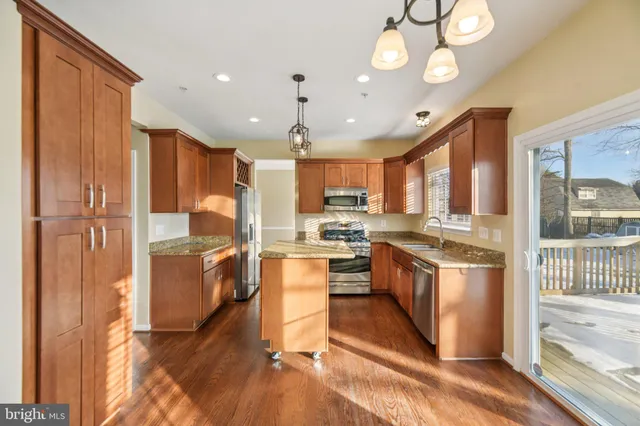 a kitchen with stainless steel appliances granite countertop a refrigerator a sink dishwasher a oven and a dining table with wooden floor