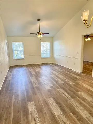 an empty room with wooden floor a ceiling fan and windows