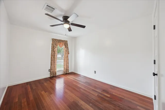 an empty room with wooden floor fan and windows