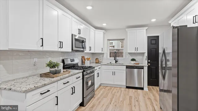a kitchen with stainless steel appliances granite countertop a stove a sink dishwasher and a refrigerator with white cabinets